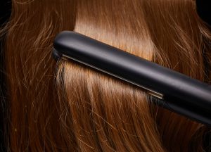 Close-up image of hair straighteners being run through shiny, light-brown hair