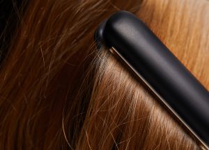 Close-up image of hair straighteners being run through shiny, light-brown hair