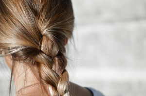 Close-up on the back of a woman's head and neck, showcasing a perfectly plaited light brown ponytail